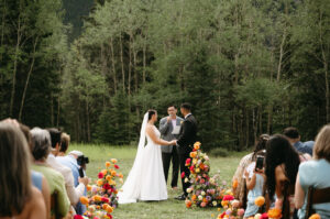 A couple at their ceremony with colourful florals, at Rundleview Parkette in Kananaskis